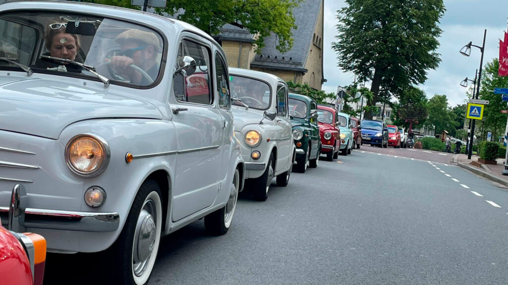 Fiat 600 Oldtimer stehen aufgereiht wie eine Perlenkette am Fahrbahnrand